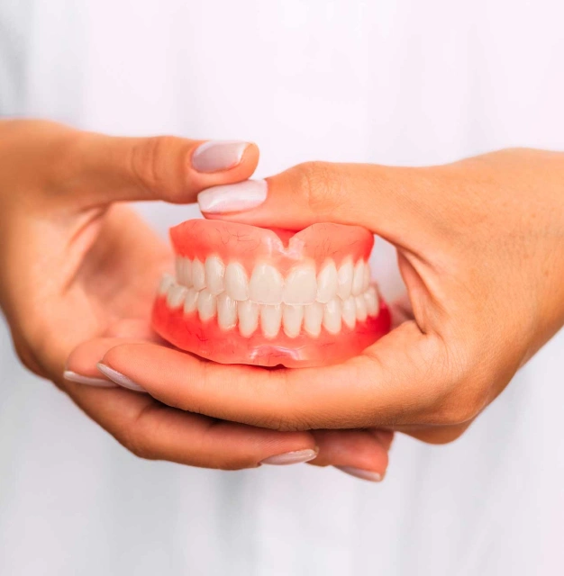 Hands holding dentures with red gums against white background for dental care display