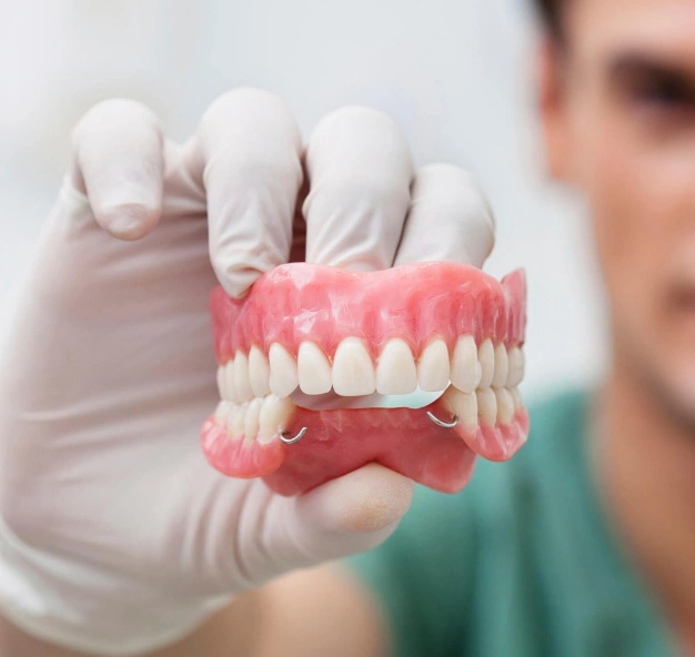 Dentist in gloves holding full denture model showing upper and lower artificial teeth.