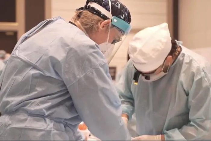 Two dental professionals in surgical attire performing a denture procedure in a clinical setting.