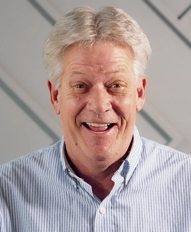 Smiling man in blue striped shirt against gray striped background, professional headshot for dental services.