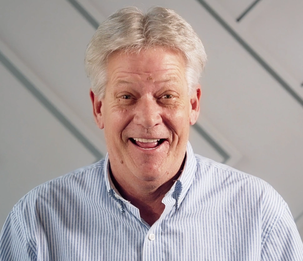 Smiling older man in light blue shirt against neutral background for Memphis dentures website